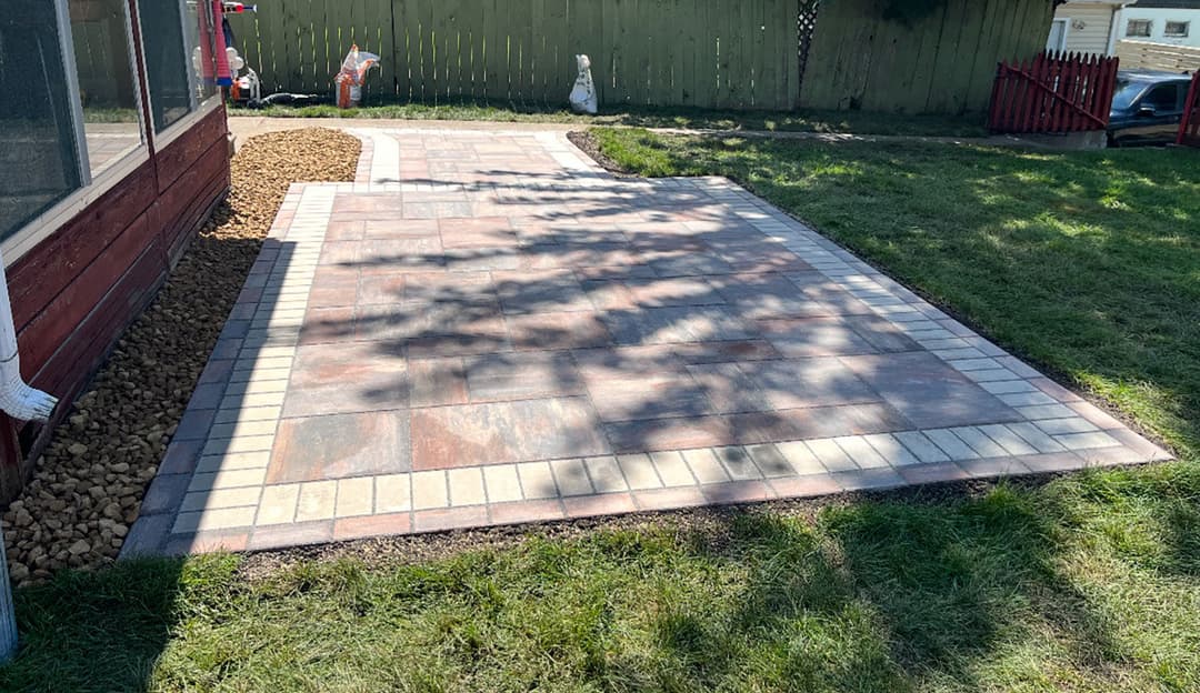 Paved outdoor patio with stone tiles and grass area, ideal for garden gatherings and relaxation.