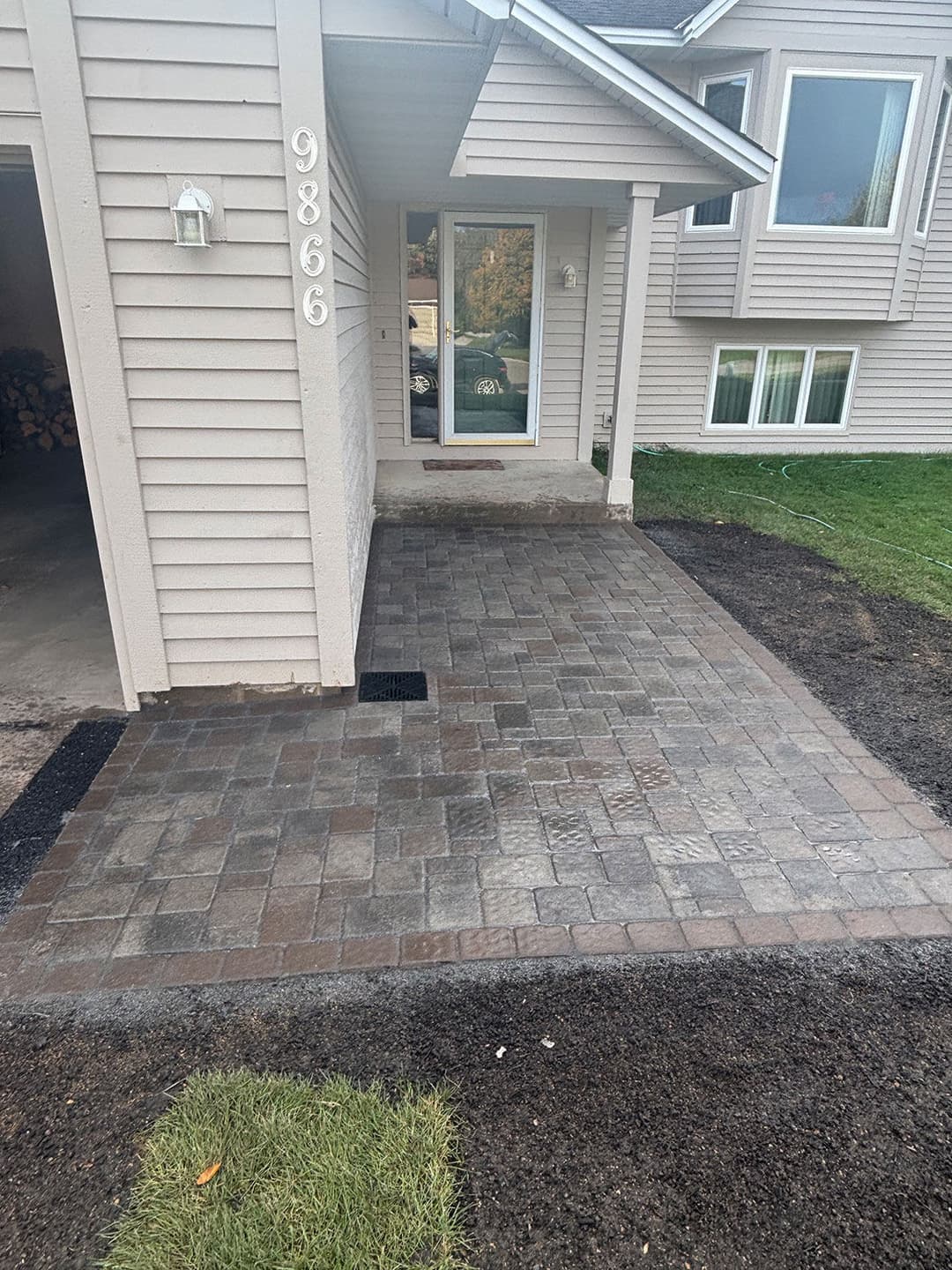 Paved entrance with decorative stones, featuring a house number and freshly landscaped yard.