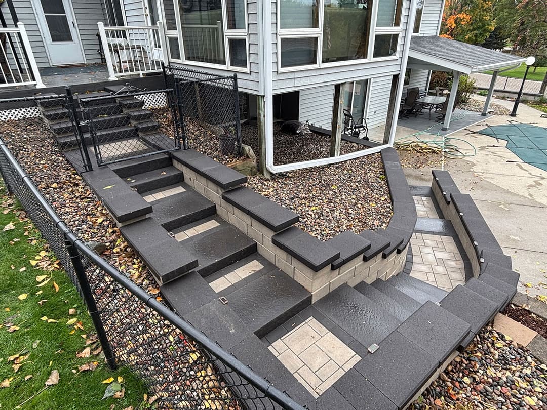 Decorative outdoor stone staircase with landing, surrounded by a fenced yard and autumn foliage.