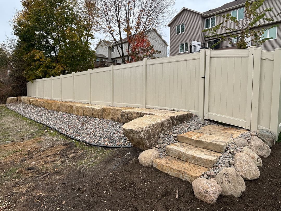 Neutral-colored vinyl fence with stone steps and gravel path in a residential yard.