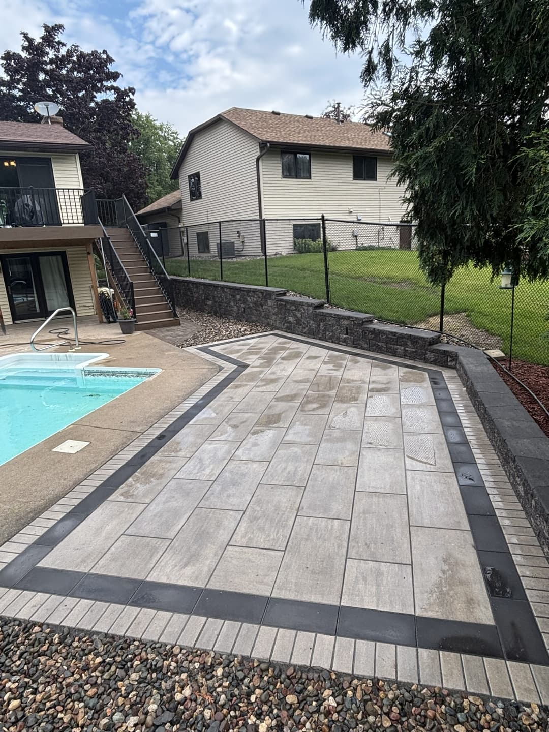 Modern outdoor patio with stone pavers, poolside, and landscaped yard in residential setting.