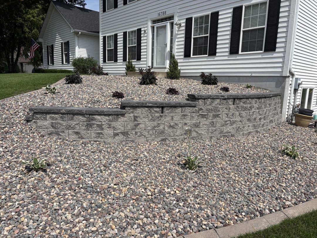 Decorative stone landscaping with gray retaining wall and low plants in front of a white house.
