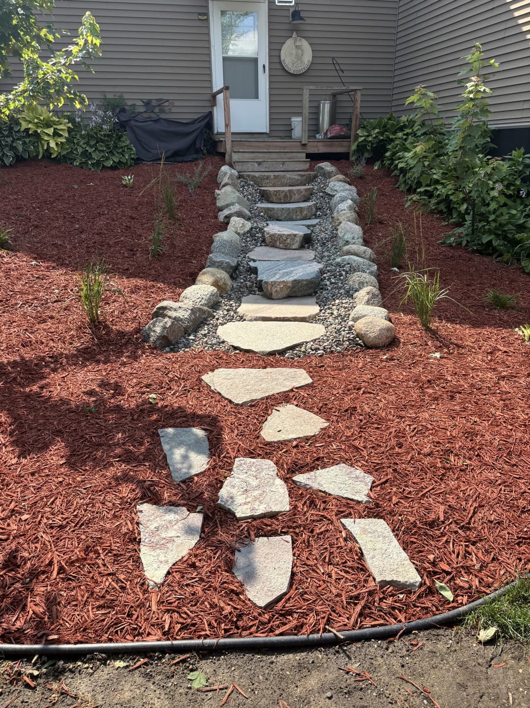 Stone path leading to a house, surrounded by red mulch and greenery.