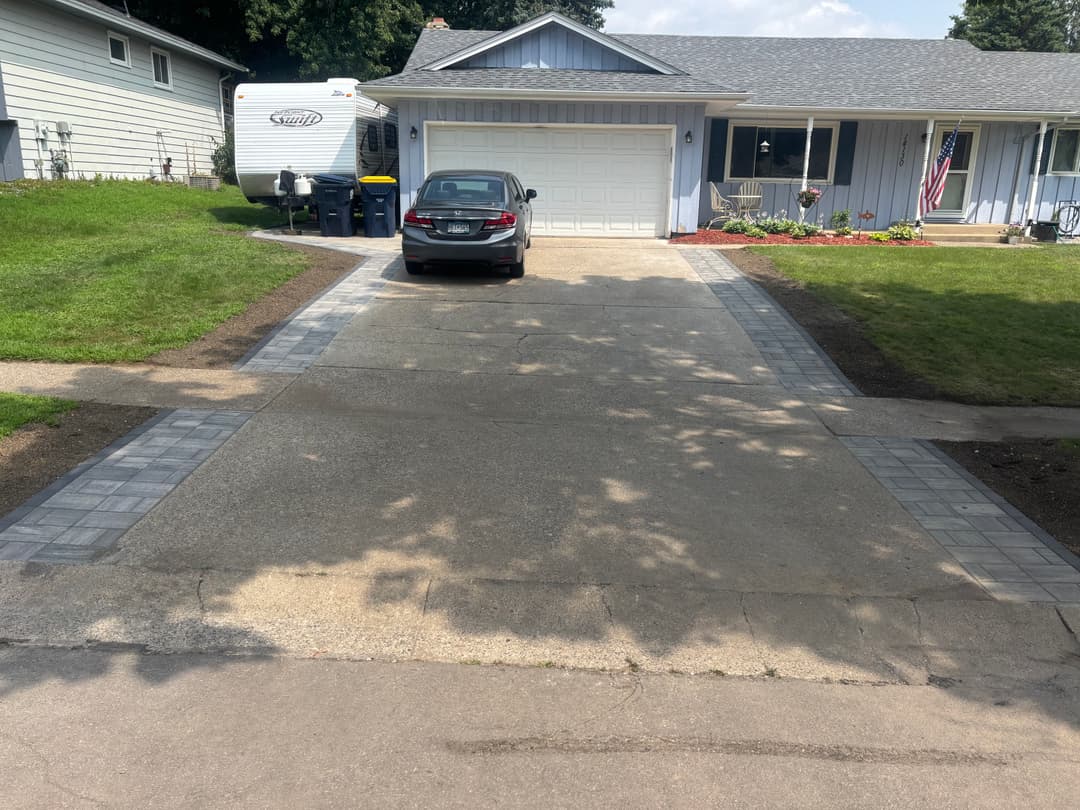 House with a gray car in driveway, lined with paver stones and green lawn.