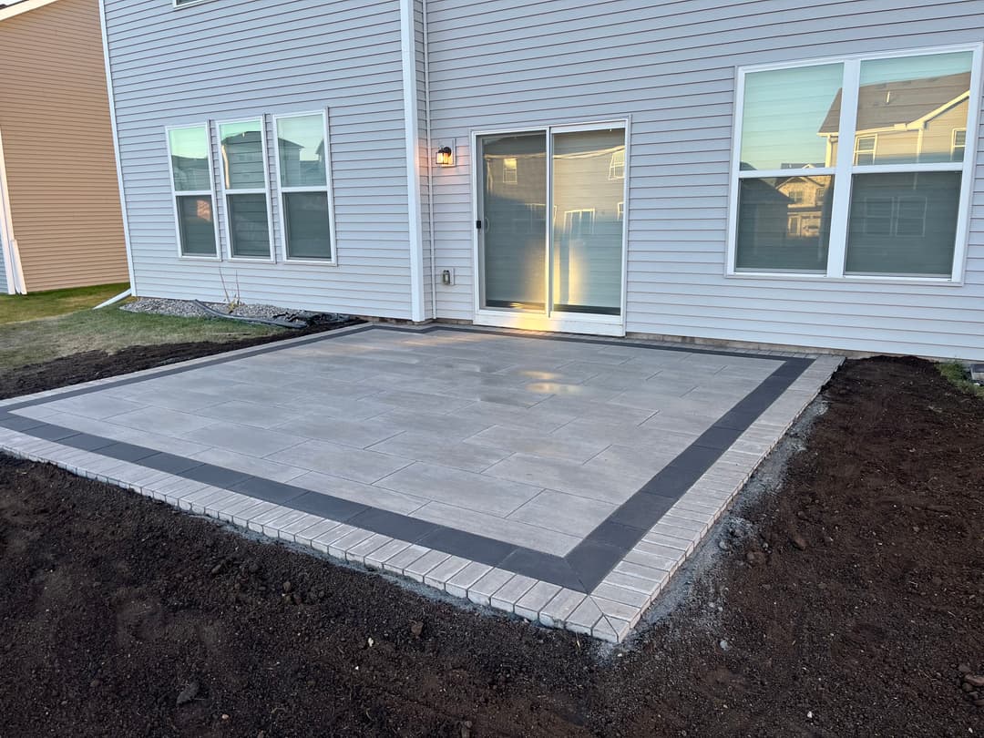 Newly installed outdoor patio with paver border and sliding glass doors in a residential setting.