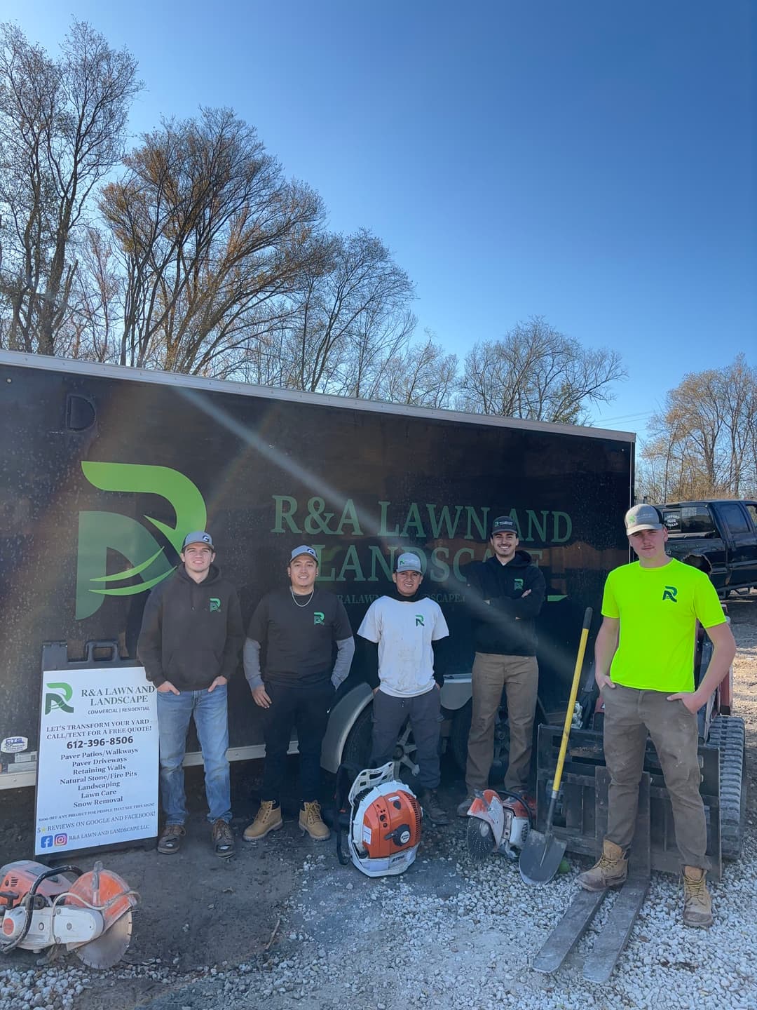 R&A Lawn and Landscape team poses by their trailer with landscaping equipment on a sunny day.