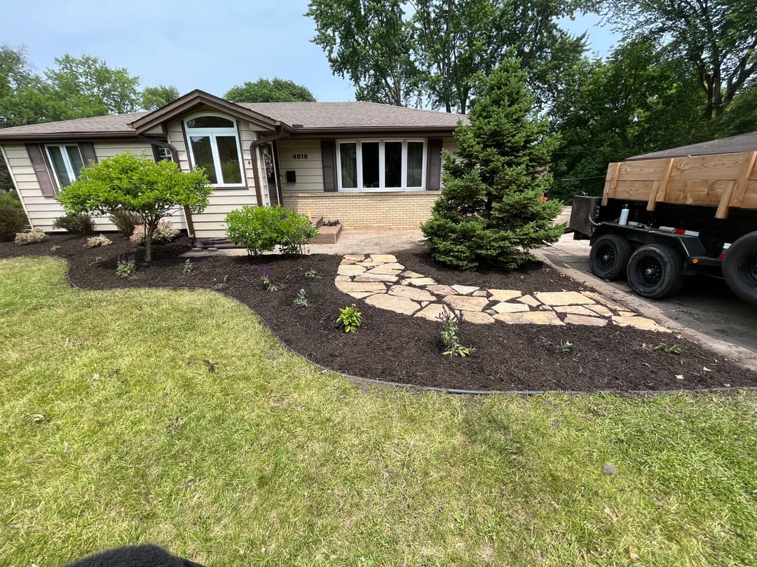 Front yard landscaping with stone path, garden plants, and freshly mulched area.
