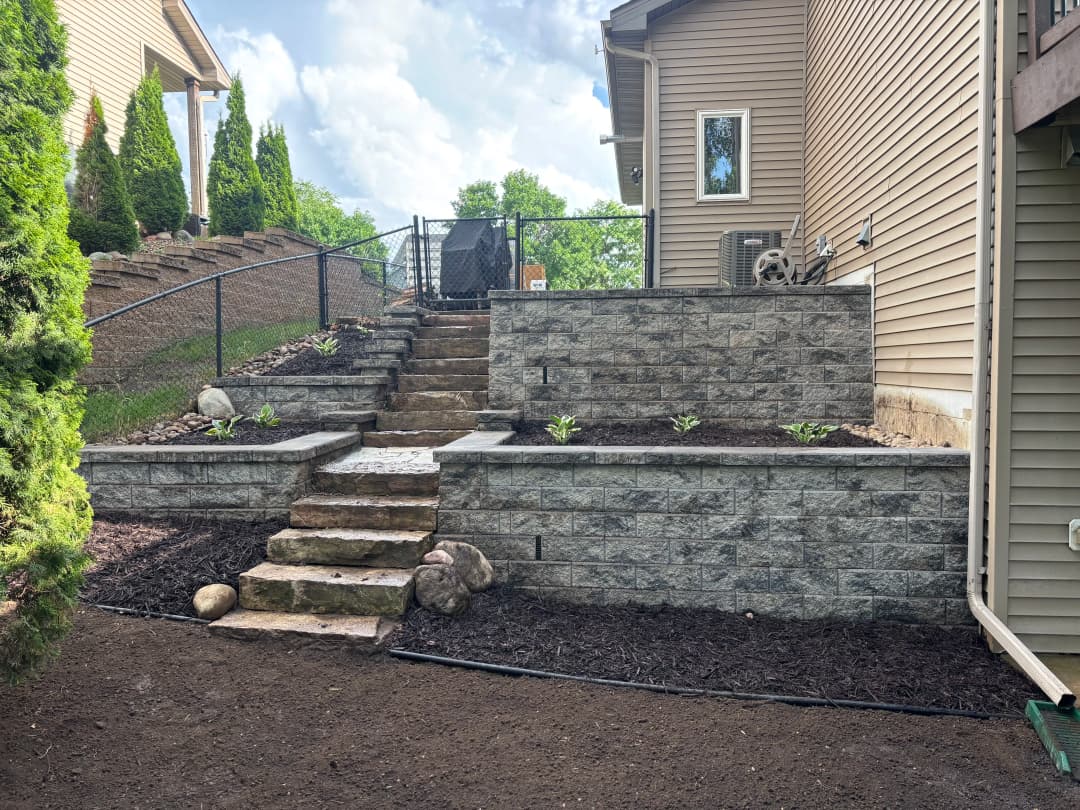Landscaped backyard with stone steps and retaining walls, featuring mulch and greenery.