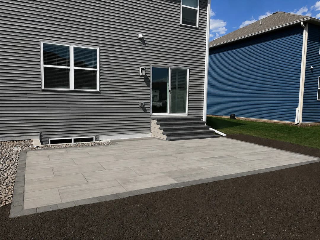 Paver patio installation behind modern gray house with steps and landscaping.