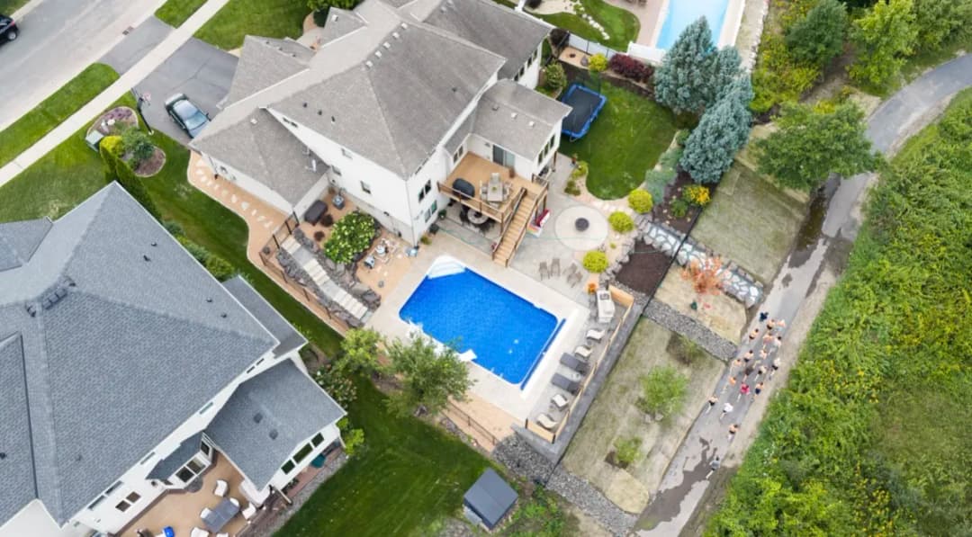 Aerial view of suburban homes with a pool, landscaped gardens, and a walking path.