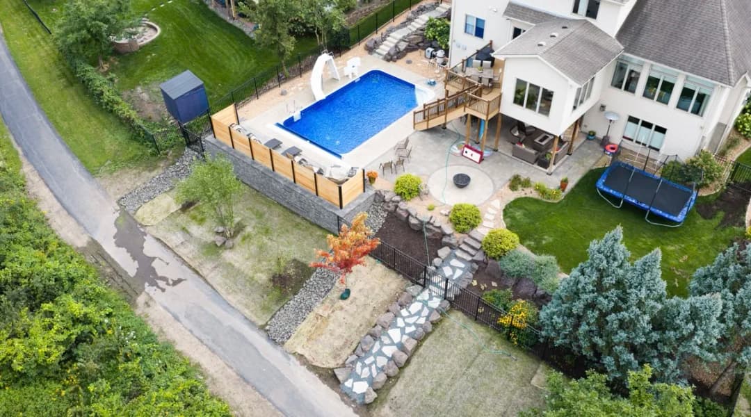 Aerial view of a backyard with a blue swimming pool, deck, and landscaped garden.