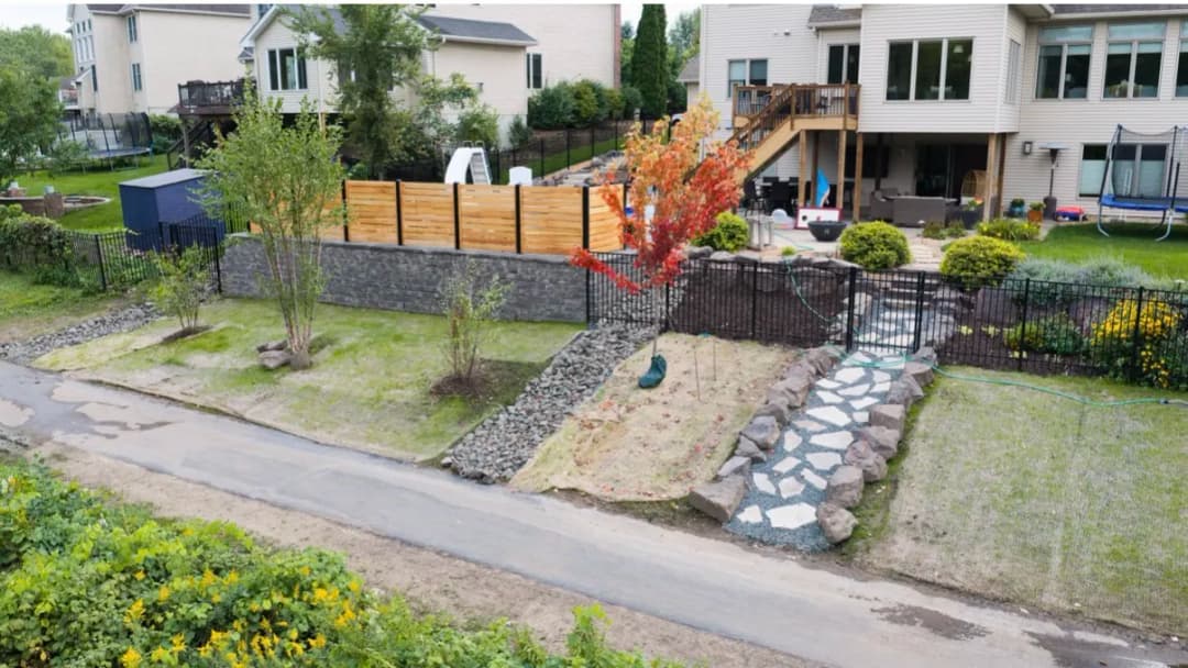 landscaped backyard with stone path, decorative trees, and a wooden fence in a suburban setting