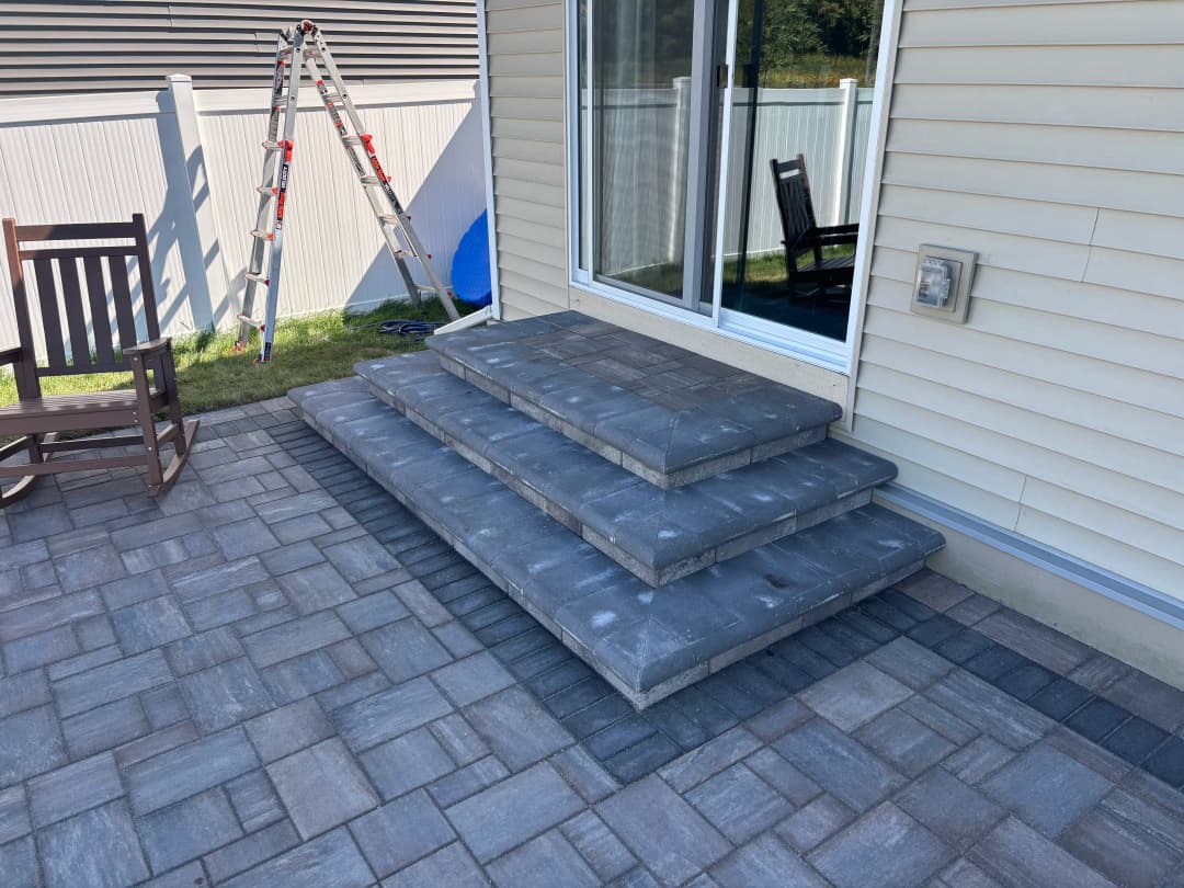 Stone steps leading to patio door, surrounded by paver stones and a ladder nearby.
